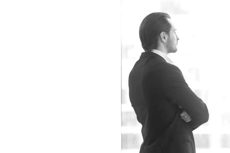Executivo de perfil diante de uma janela, em contraluz, olhando para a linha que divide os dois painéis.
